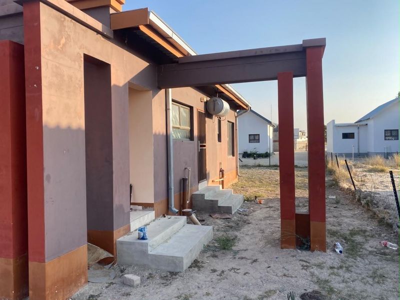 Rear exterior view of the property featuring concrete steps, an external electric geyser, and a pergola structure, set against an unlandscaped yard.