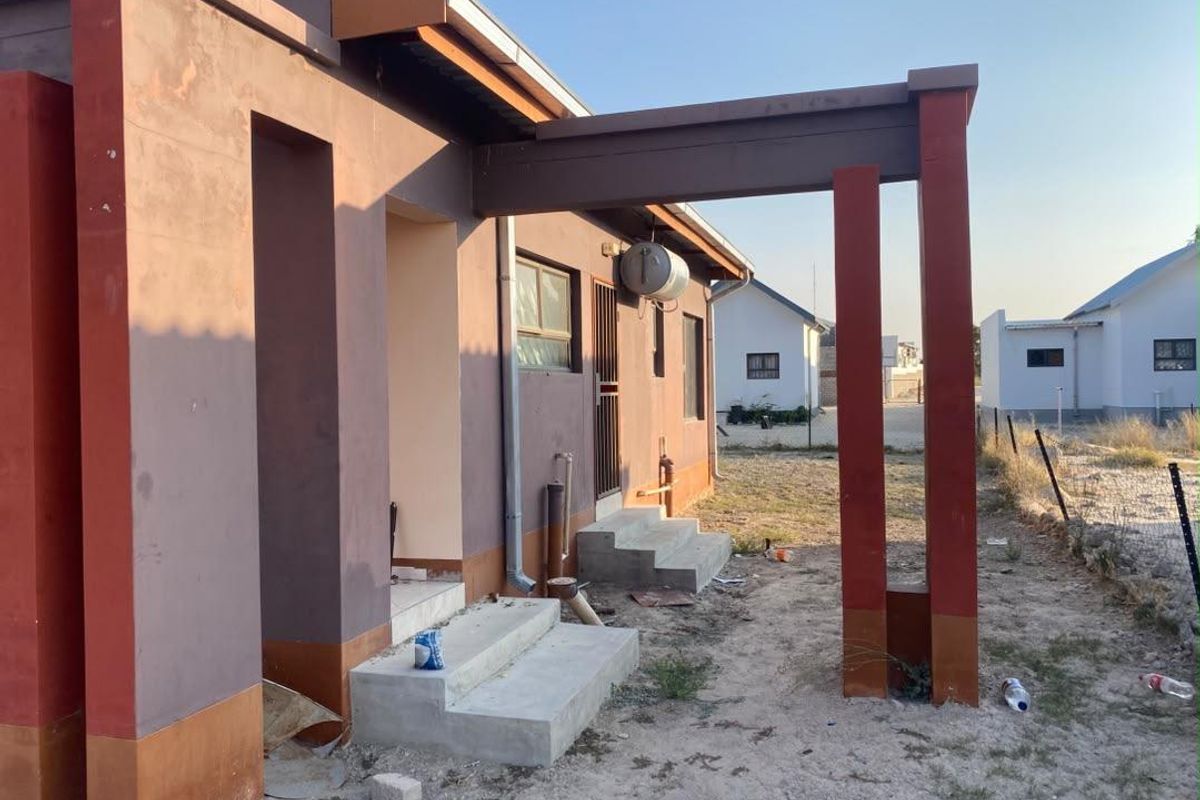 Rear exterior view of the property featuring concrete steps, an external electric geyser, and a pergola structure, set against an unlandscaped yard.