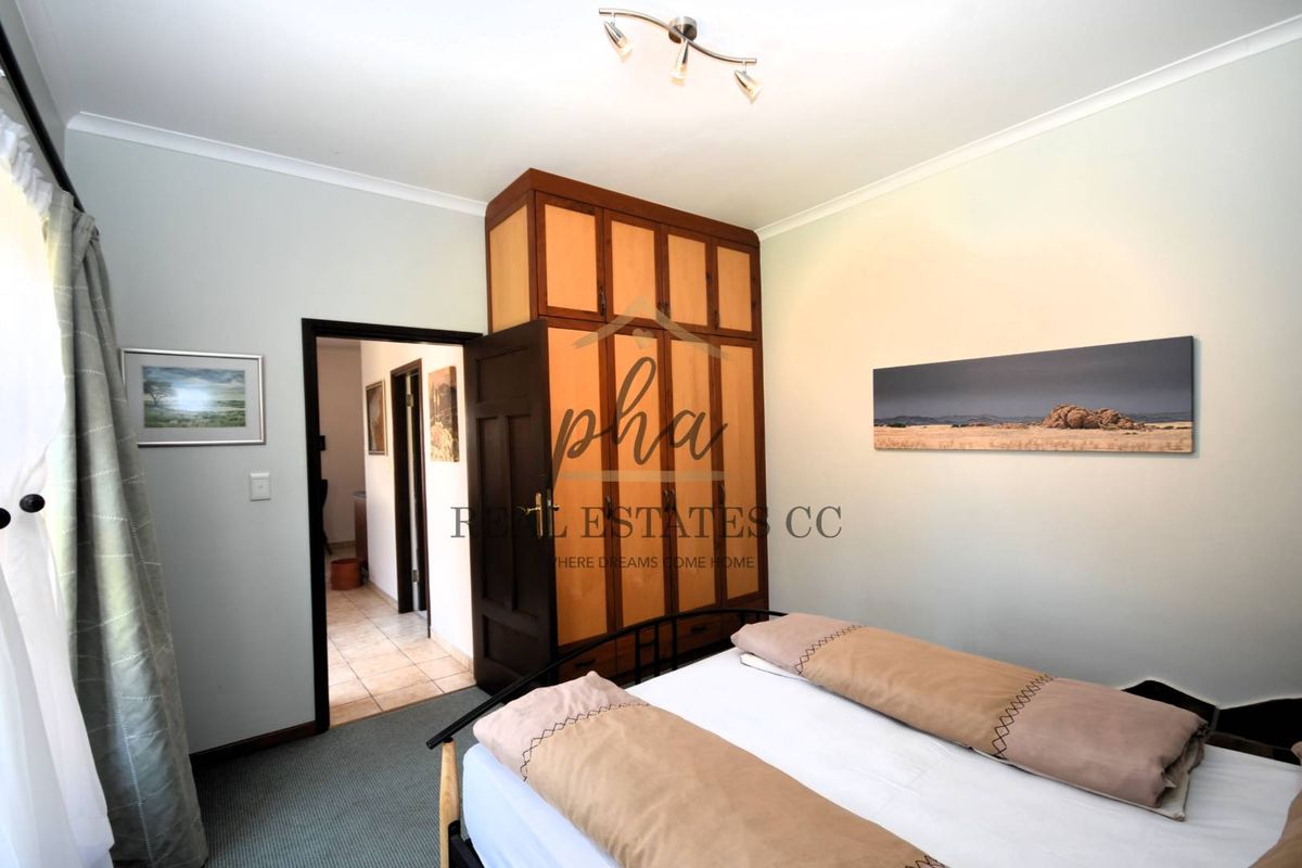 A bedroom featuring built-in wooden cupboards and carpeted flooring, with an adjacent hallway visible through the doorway.