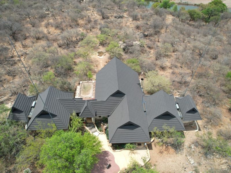 Aerial view of a residential property featuring a large pitched roof, integrated swimming pool, and surrounding natural bushveld landscape.