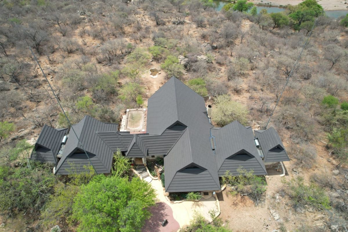 Aerial view of a residential property featuring a large pitched roof, integrated swimming pool, and surrounding natural bushveld landscape.