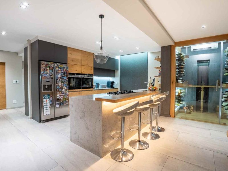 Modern kitchen featuring a central island with breakfast bar, high-end built-in appliances, and a glass-enclosed climate-controlled wine cellar.