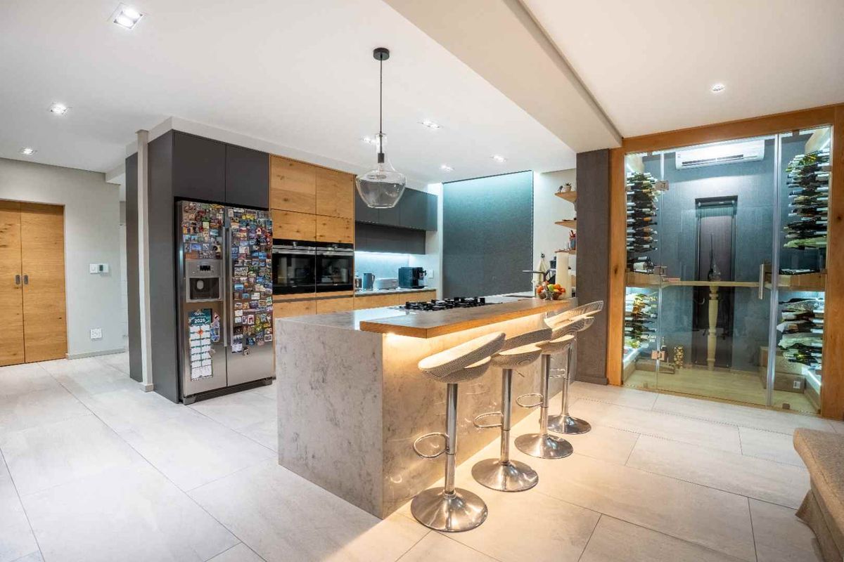 Modern kitchen featuring a central island with breakfast bar, high-end built-in appliances, and a glass-enclosed climate-controlled wine cellar.