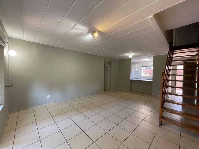 An open-plan living area featuring tiled flooring, a wooden staircase, and a pass-through window connecting to the kitchen space.