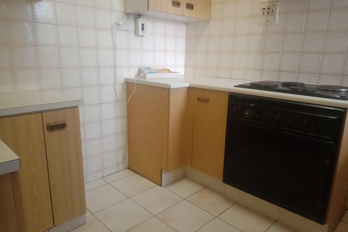 A compact kitchen featuring dated laminate cabinetry, tiled splashbacks, and a built-in electric oven and hob, offering potential for a modern renovation.