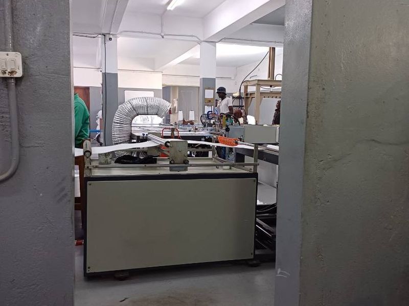 Industrial workspace featuring exposed structural beams, fluorescent lighting, and heavy-duty manufacturing equipment within a functional commercial facility.