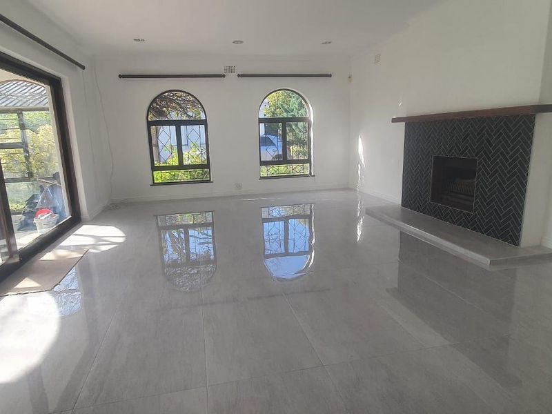 Spacious, light-filled living room featuring large format floor tiles, a modern fireplace with herringbone tiling, and seamless access to the outdoor patio area.