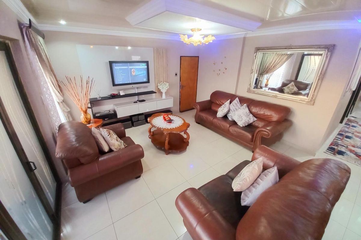 A well-maintained living room featuring tiled flooring, a recessed ceiling detail with integrated lighting, and a built-in media wall unit.