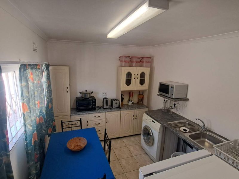 A functional kitchen featuring built-in cabinetry, laminate countertops, a double bowl stainless steel sink, and tiled flooring, with space for laundry appliances.