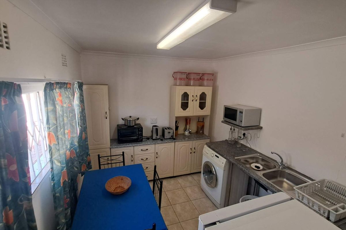 A functional kitchen featuring built-in cabinetry, laminate countertops, a double bowl stainless steel sink, and tiled flooring, with space for laundry appliances.