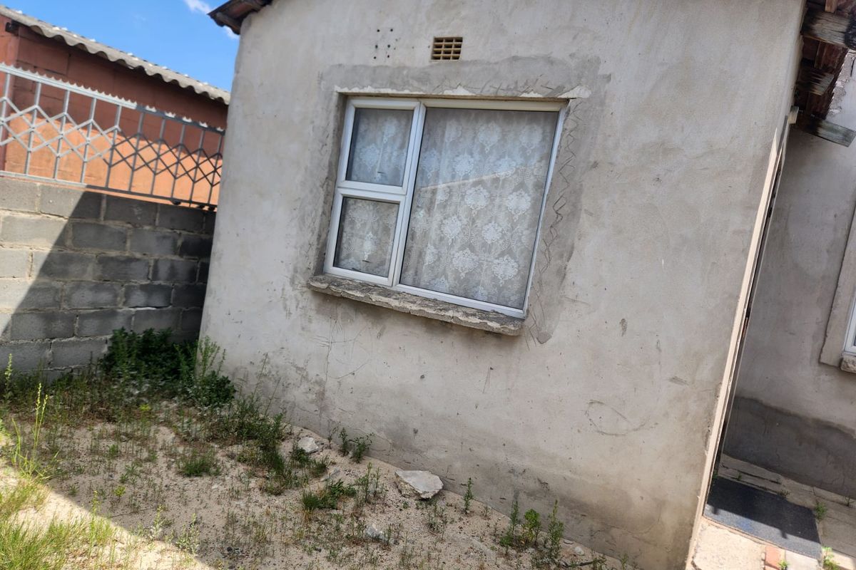 Exterior view of the rear building facade featuring an aluminium window, unfinished plaster walls, and a concrete block boundary wall with security fencing.
