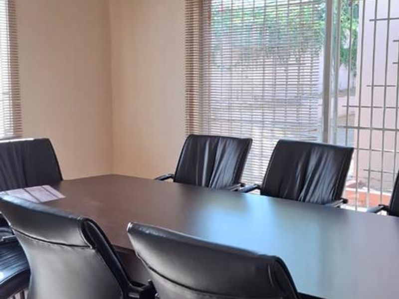 A functional office space featuring tiled flooring, large windows with venetian blinds, and a sliding glass door with security bars.