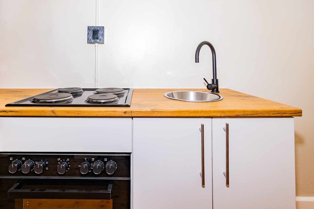 Compact kitchenette featuring a wooden countertop, integrated electric hob, built-in oven, and a small stainless steel sink with a modern black faucet.