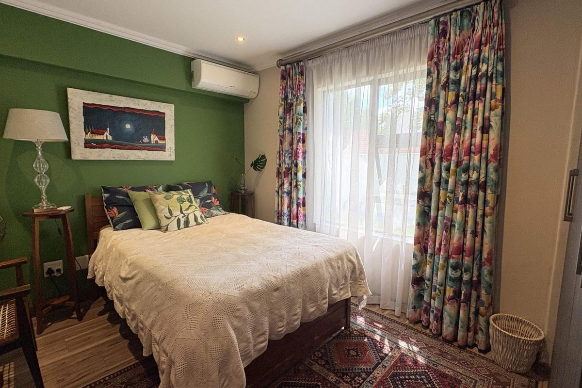 A cozy bedroom featuring a green accent wall, built-in air conditioning unit, and large window with floor-to-ceiling curtains.