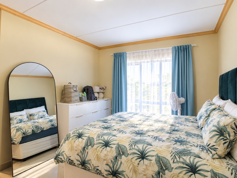 A well-lit bedroom featuring neutral walls, crown molding, tiled flooring, and a large window with curtains, providing a comfortable and bright living space.