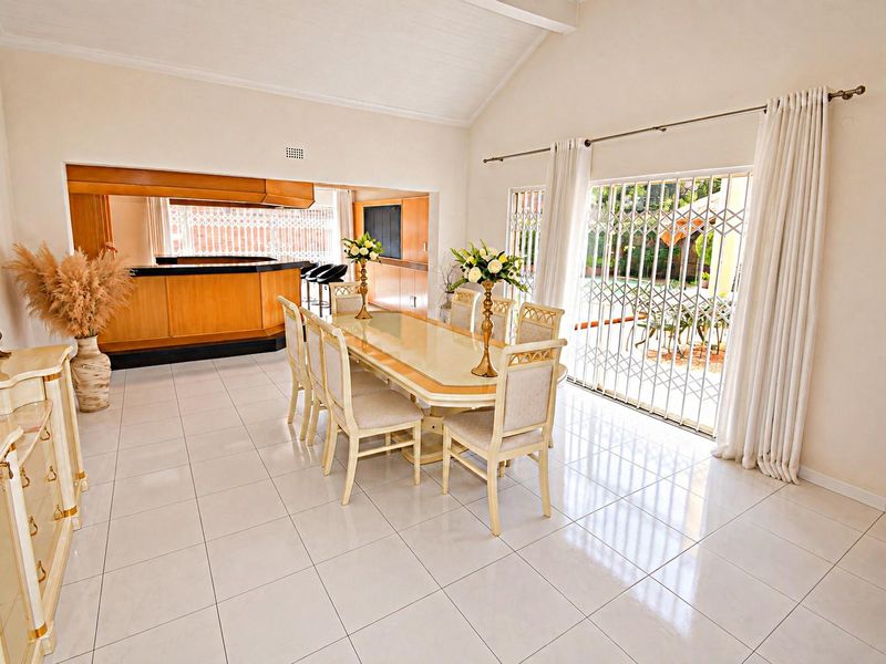Spacious open-plan dining area featuring vaulted ceilings, tiled flooring, and a built-in bar, with direct access to the garden through sliding security doors.