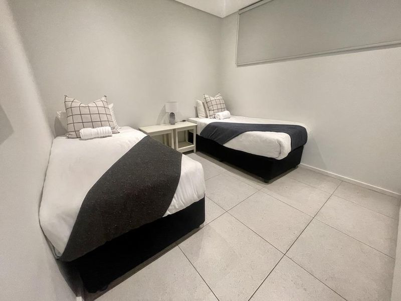 A clean and modern bedroom featuring neutral wall tones, large format floor tiles, and a fitted roller blind.