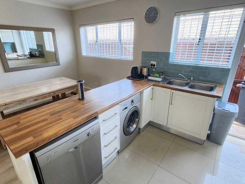 A functional kitchen featuring wooden countertops, white cabinetry, a double stainless steel sink, and integrated laundry and dishwasher appliances with tiled flooring.