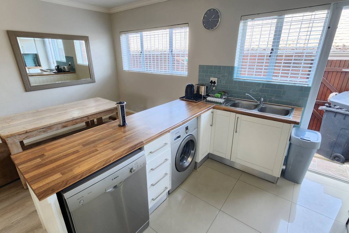 A functional kitchen featuring wooden countertops, white cabinetry, a double stainless steel sink, and integrated laundry and dishwasher appliances with tiled flooring.