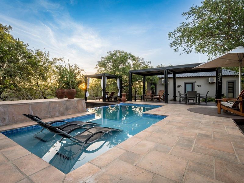 A well-maintained outdoor pool area featuring a tiled deck, integrated swimming pool, and a covered patio space, perfect for relaxation in a natural setting.