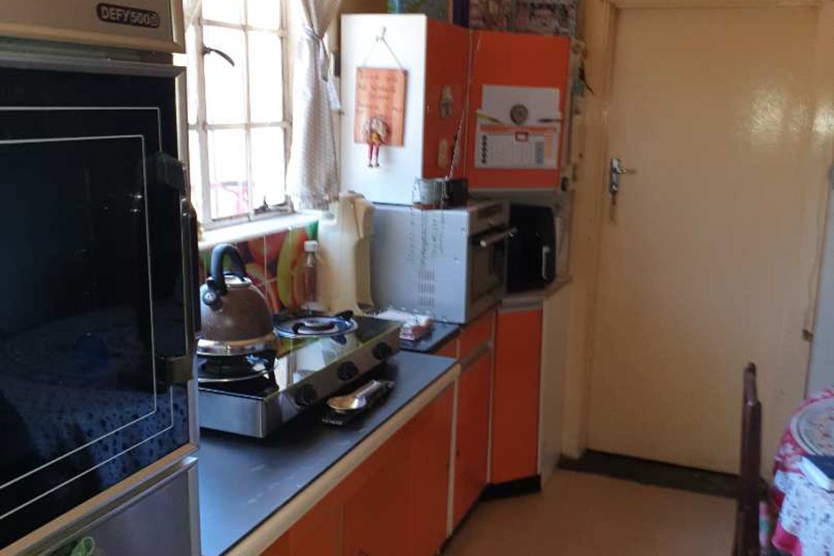 A dated kitchen featuring orange cabinetry, a built-in Defy oven, and a compact workspace with a window overlooking the exterior.