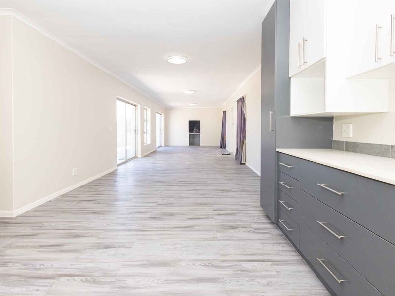 Spacious open-plan living area featuring modern grey and white cabinetry, laminate flooring, and sliding glass doors leading to the exterior.