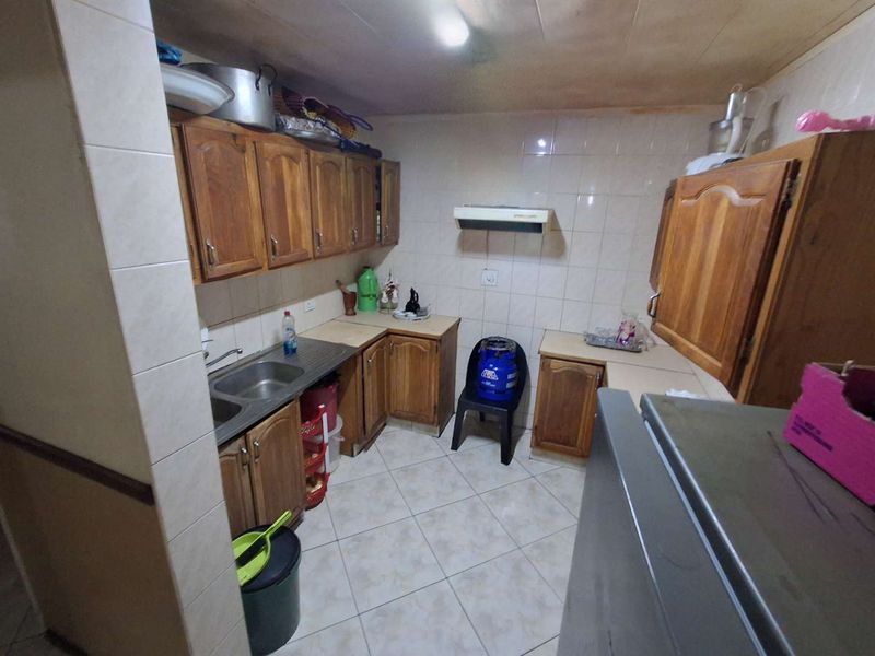 A functional kitchen featuring wooden cabinetry, tiled splashbacks, and a double bowl stainless steel sink, offering potential for modernization.