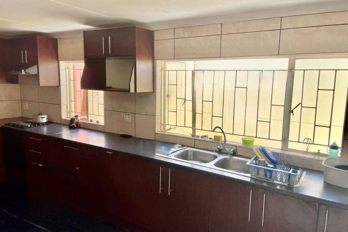 A functional kitchen featuring dark wood cabinetry, a double basin sink, tiled backsplash, and large windows with security bars.
