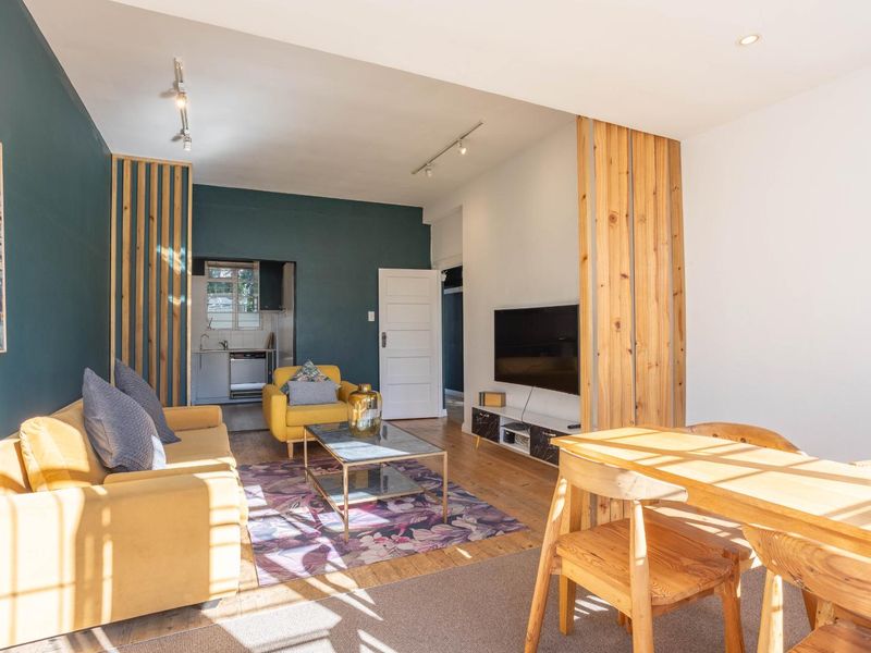Open-plan living and dining area featuring timber slat room dividers, hardwood flooring, and modern track lighting, with an adjacent kitchen visible.