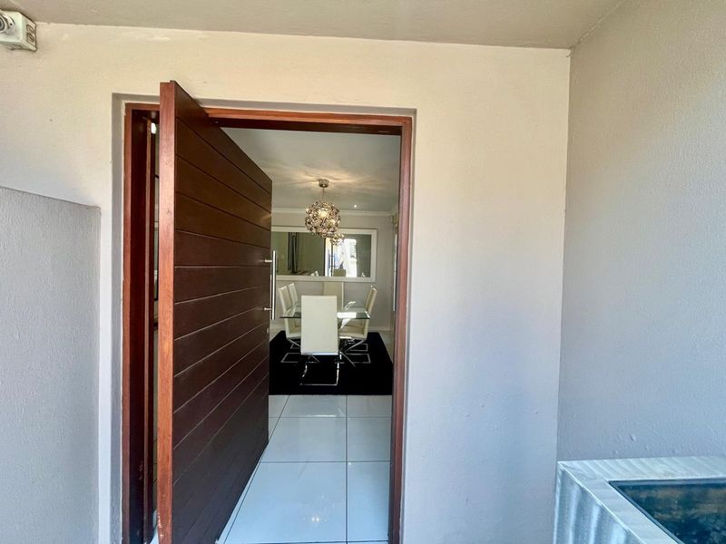 A welcoming entrance featuring a solid timber front door leading into a bright, tiled interior space with modern lighting.