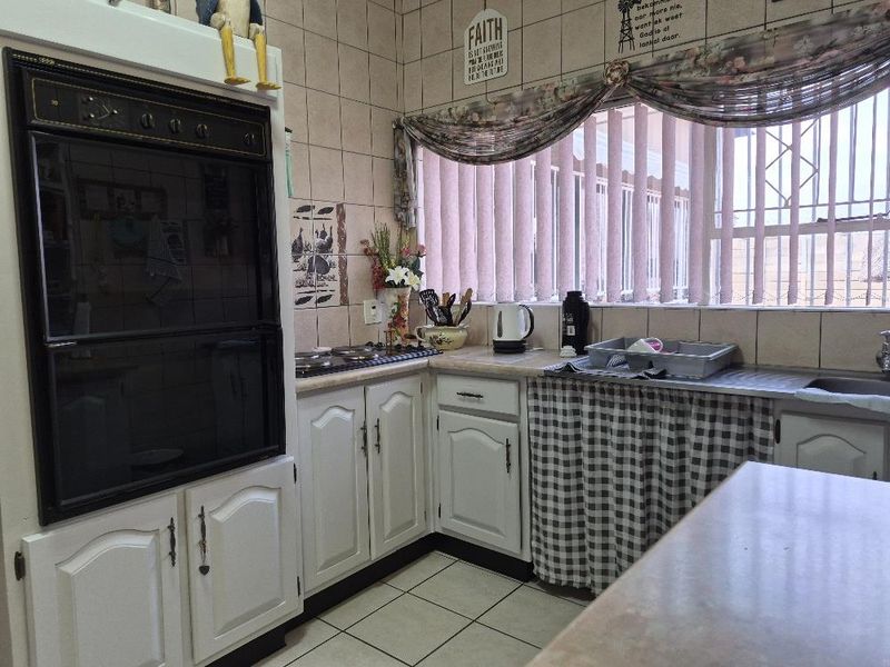 A functional kitchen featuring built-in cabinetry, an integrated oven, electric hob, and tiled surfaces, offering a practical layout with natural light.