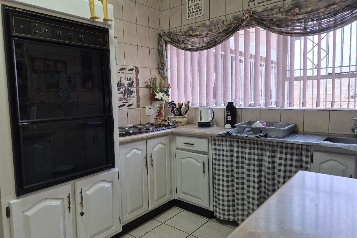 A functional kitchen featuring built-in cabinetry, an integrated oven, electric hob, and tiled surfaces, offering a practical layout with natural light.