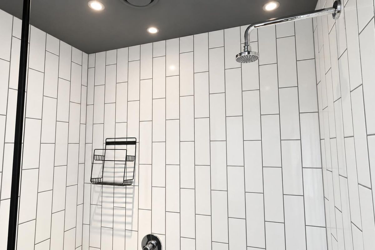 Modern walk-in shower featuring clean white subway tiling, a contemporary shower head, and recessed ceiling lighting.
