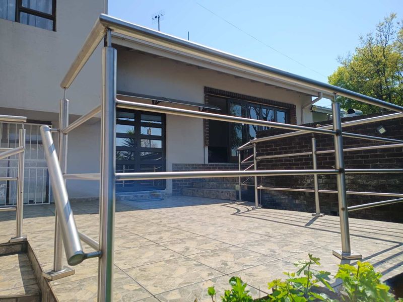 A paved outdoor patio area featuring a modern stainless steel balustrade, brick retaining wall, and access to the home via glass sliding doors.