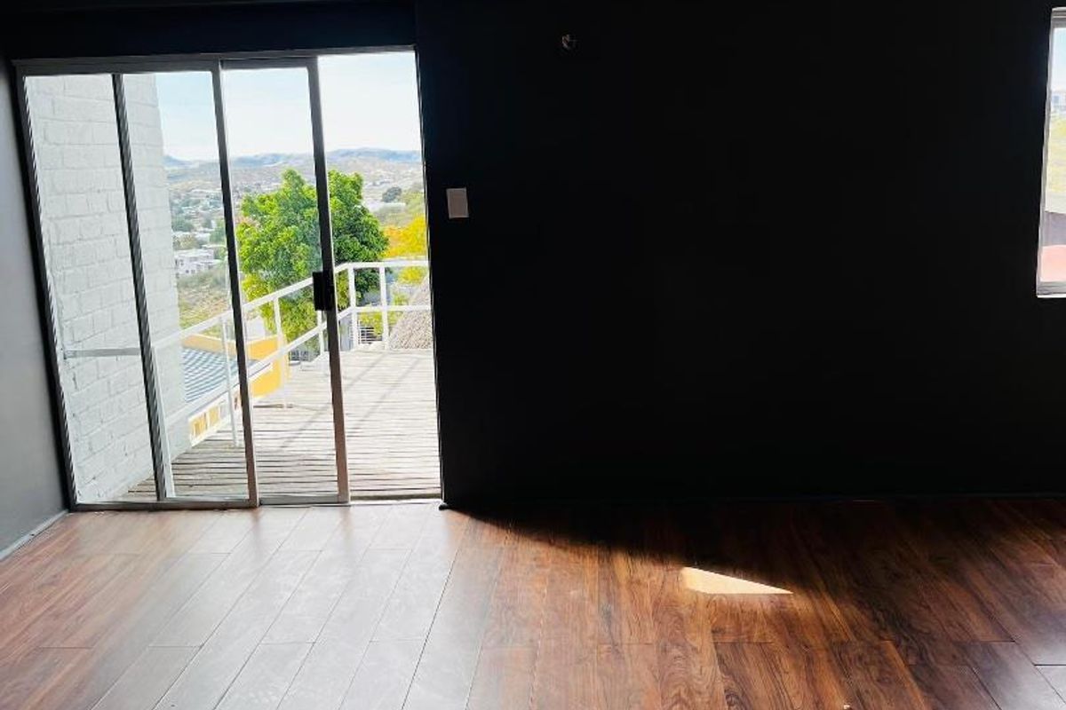 An empty living room featuring dark accent walls, wood-look laminate flooring, a wall-mounted air conditioning unit, and sliding glass doors leading to a balcony.