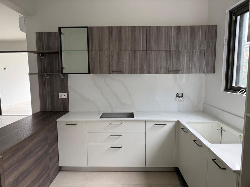 Modern kitchen featuring two-tone cabinetry, stone-look countertops, integrated cooktop, and a built-in sink with contemporary finishes.