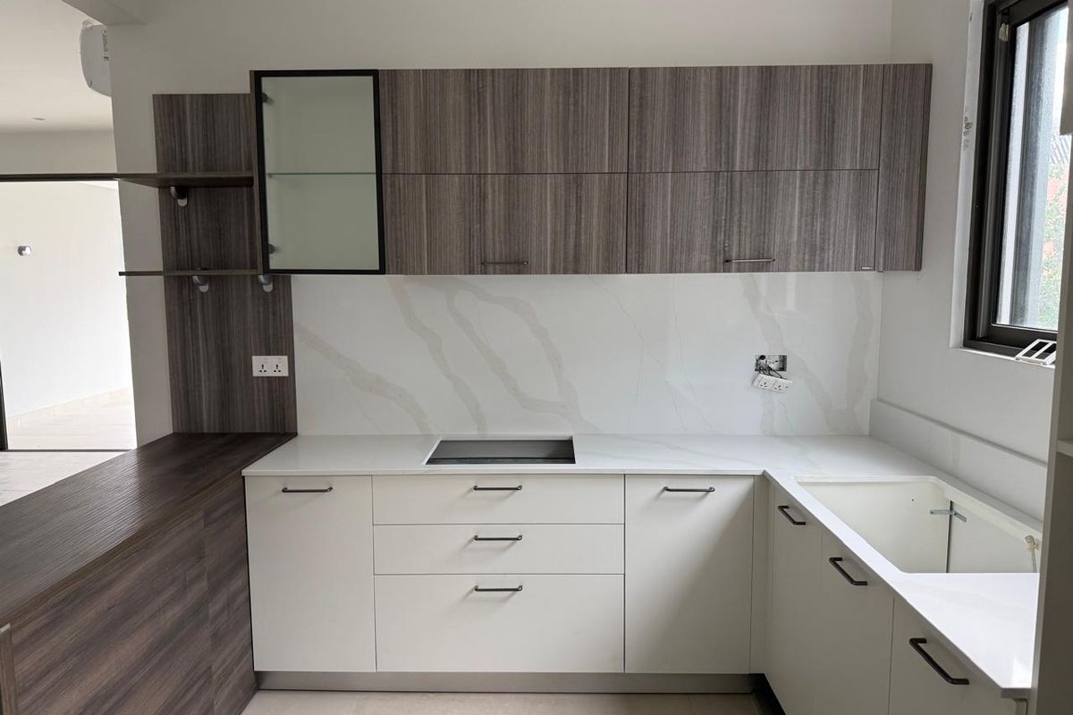 Modern kitchen featuring two-tone cabinetry, stone-look countertops, integrated cooktop, and a built-in sink with contemporary finishes.