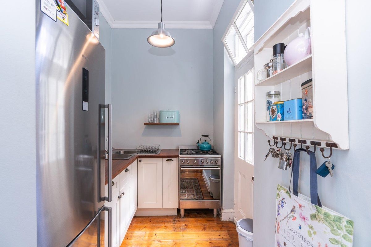 A compact, functional kitchen featuring wooden countertops, white cabinetry, a gas stove, and original timber flooring, providing an efficient workspace.