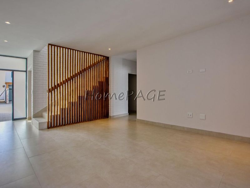 Spacious open-plan living area featuring modern tiled flooring, a striking timber slat staircase partition, and direct access to the exterior.