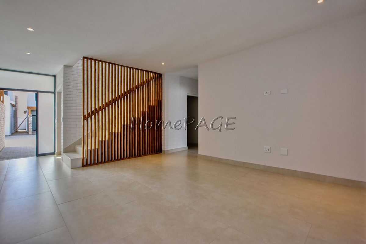 Spacious open-plan living area featuring modern tiled flooring, a striking timber slat staircase partition, and direct access to the exterior.