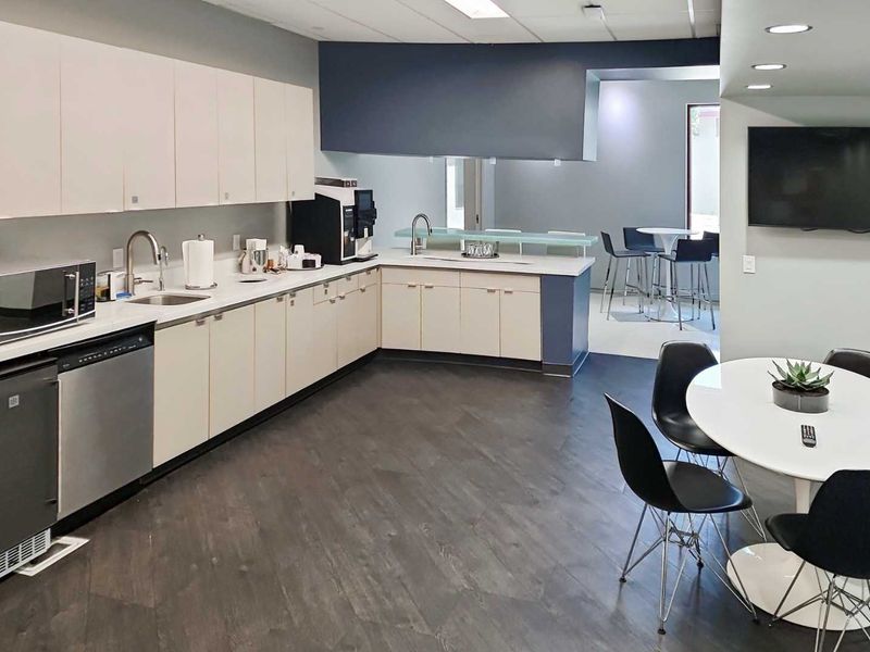 Modern office kitchenette featuring sleek cabinetry, stainless steel dishwasher, integrated sink, and durable flooring, providing a functional break area for staff.