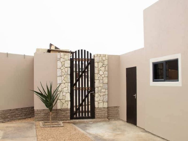 A front exterior view featuring a concrete driveway, gravel pathway, stone-clad gate entrance, and boundary walls with a side access door.