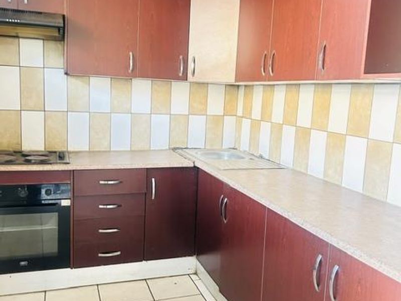 A dated kitchen featuring dark laminate cabinetry, built-in oven, electric hob, and tiled splashbacks, offering a functional layout ready for modernization.