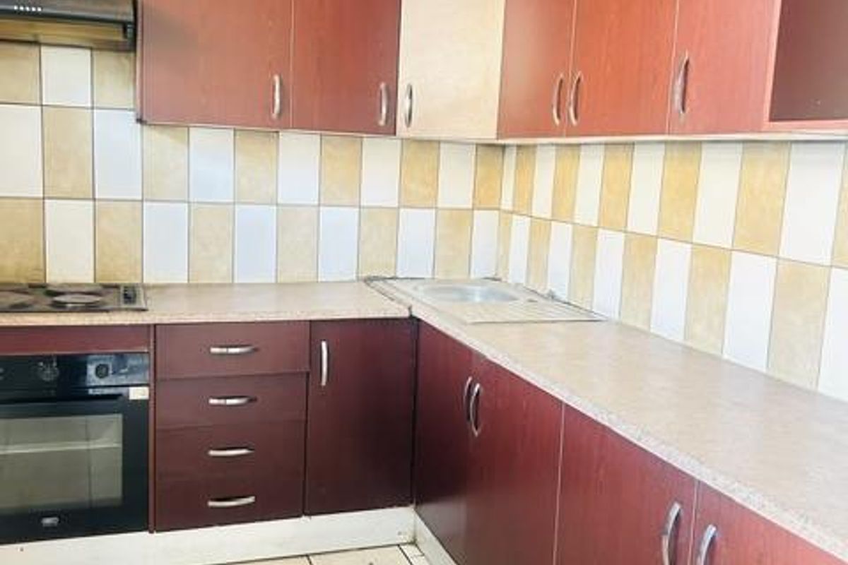 A dated kitchen featuring dark laminate cabinetry, built-in oven, electric hob, and tiled splashbacks, offering a functional layout ready for modernization.