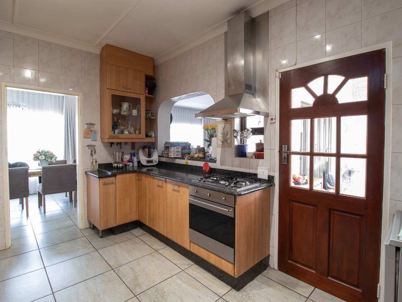 A functional kitchen featuring wooden cabinetry, granite countertops, integrated stainless steel appliances, and tiled finishes, with direct access to the dining area.