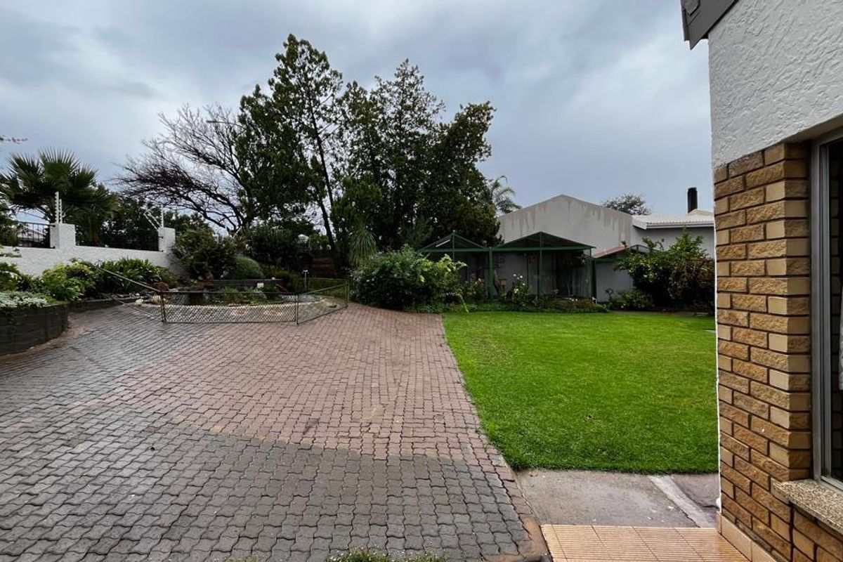 A spacious rear garden featuring a paved patio area, a well-maintained lawn, and established perimeter landscaping with a small pond enclosure.