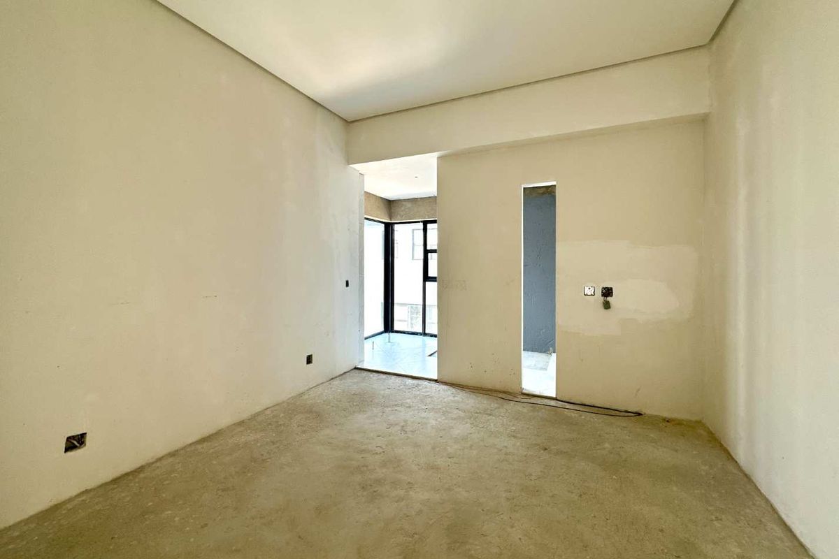 An unfinished bedroom space featuring raw concrete floors, plastered walls, and black aluminium window frames, awaiting final flooring and decorative finishes.