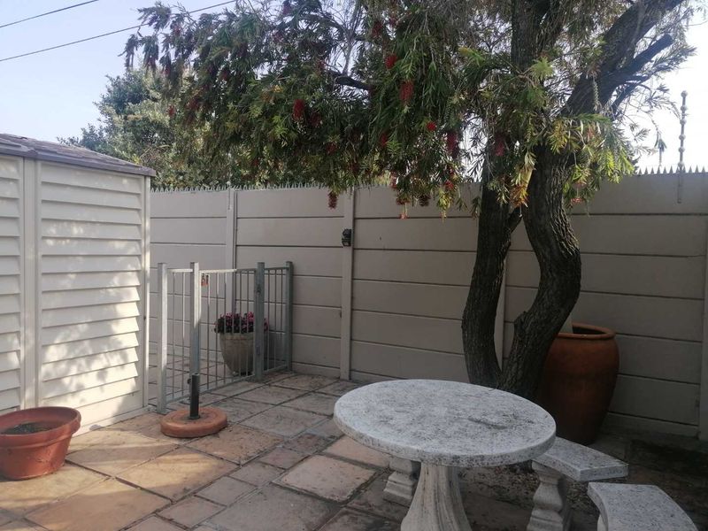 A paved outdoor patio area featuring a precast concrete boundary wall with security spikes, a metal gate, and a small storage shed.