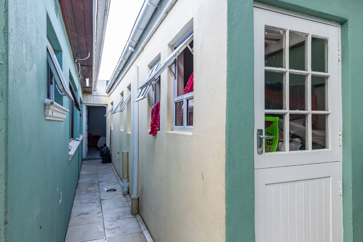 A narrow exterior side passage featuring tiled flooring, guttering, and a stable door, providing access between building sections.
