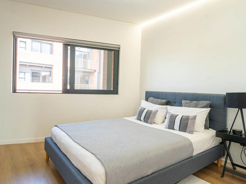 A modern, well-lit bedroom featuring laminate flooring, neutral walls, and a large sliding window providing natural light.